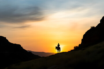 Fototapeta premium A quiet canyon, with the silhouette of a horse rider against a glowing sunset.