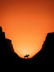 A quiet canyon, with the silhouette of a horse rider against a glowing sunset.


