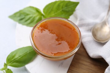 Tasty curry sauce in glass bowl and basil on white table, closeup
