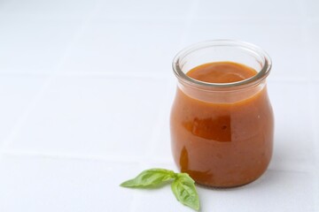 Tasty curry sauce in glass jar and basil on white tiled table, closeup. Space for text