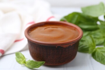 Tasty curry sauce and basil leaves on white tiled table, closeup