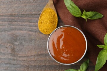 Tasty curry sauce in metal dish, powder and basil on wooden table, flat lay. Space for text