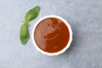 Tasty curry sauce and basil leaves on grey table, top view