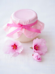 A delicate pink cream jar nestled amidst blooming cherry blossoms, bathed in soft, warm light, exuding elegance and natural beauty.