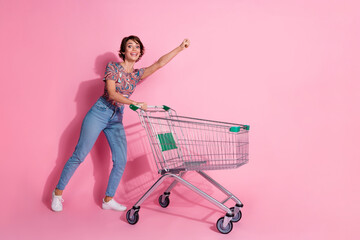 Photo of charming cheerful girl wear stylish clothes hold cart raise fist isolated on pink color...