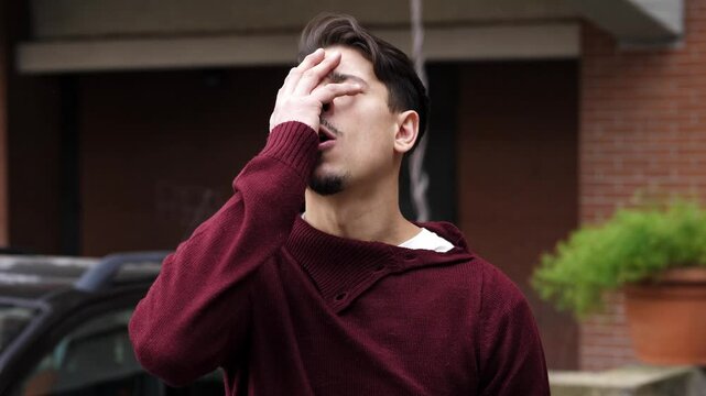 A young man suddenly remembers something sad, placing his hand on his forehead and closing his eyes, visibly affected by the emotional weight