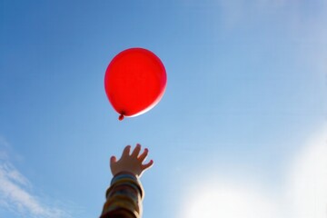 child reaching towards red balloon in blue sky, symbolizing freedom, childhood dreams, letting go, hope, or change. ideal image for concepts related to joy, aspiration, imagination