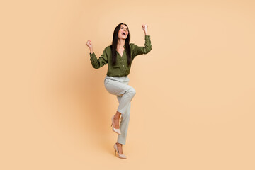 Cheerful businesswoman celebrating success in a green blouse and professional attire against a neutral beige background