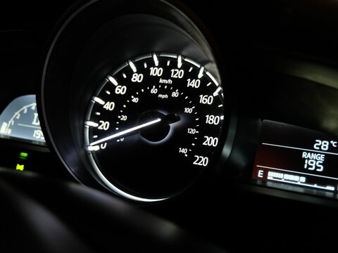 Illuminated car speedometer showing kilometers per hour, captured at night with dashboard details and digital display.