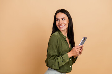 Naklejka premium Smiling businesswoman holding a smartphone against a beige background, exuding professionalism and positivity.