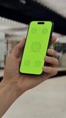 GREEN SCREEN CHROMA KEY Hand holding smartphone at a subway station with train in background, ideal for app or advertisement mockups on a transit theme