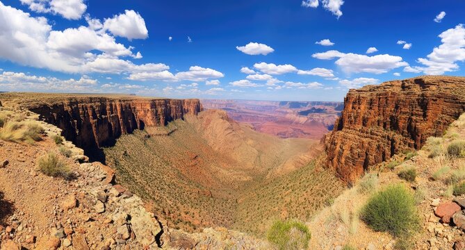 A panoramic view of a deep canyon with layered rock formations, a blue sky with fluffy clouds, and a desert landscape