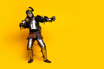 Fototapeta premium Young man in medieval armor displaying a humorous pose on a vibrant yellow background