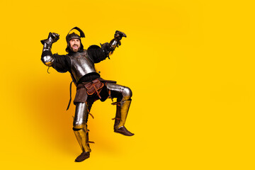Excited young man wearing medieval armor posing against bright yellow background