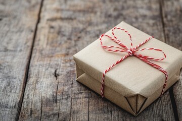 A charming rustic wrapped gift box with red twine bow sits on a textured wooden table. This cozy atmosphere highlights the joy of giving and celebration.
