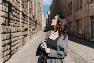 A stylish woman observes the surrounding architecture while strolling down a cobblestone street on...