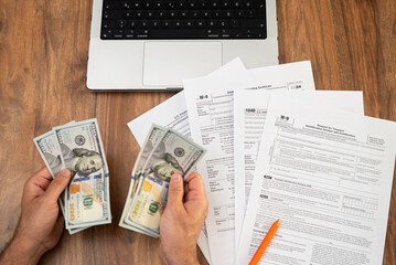 Obraz premium Male entrepreneur holds dollar banknotes in hands counting cash for filling different tax forms in accordance with strict requirements sitting at workplace with laptop