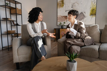 Two businesswomen discussing sitting on comfortable armchairs in modern office