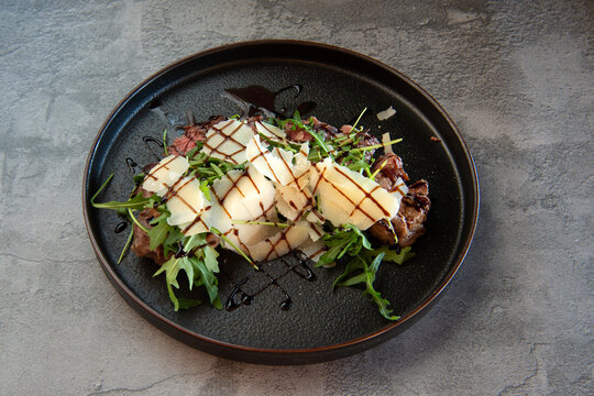 Tagliata di manzo con rucola e grana or sliced ​​beef with rocket and parmesan cheese on grey background
