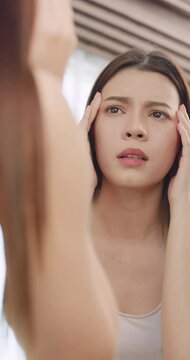 Vertical clip. Young woman worried about the wrinkles on her face while looking in the mirror at home.