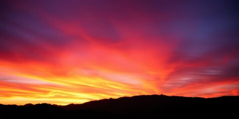 Obraz premium Fiery orange and purple sunset over silhouetted mountains, horizon, evening