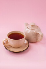 Black tea in a beige cup with a milk jug isolated on the pink background	