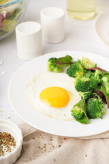 Plate with tasty fried egg, broccoli and spinach on light background