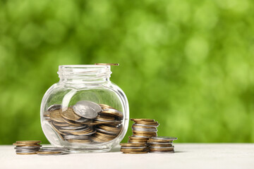 Jar with coins on table against blurred green nature background. Savings concept