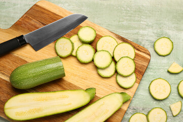 Board with slices of fresh zucchini on green wooden background