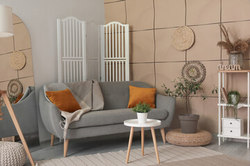 Interior of living room with grey sofa, coffee table and houseplant on wicker pouf