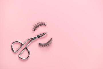 Eyelash curler in the form of scissors and two false eyelashes on pink background.