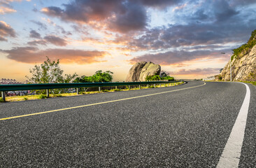 Curving asphalt highway road along a rocky hill with beautiful sunset sky background.