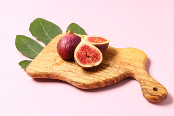 Wooden board with ripe fresh figs and plant leaf on pink background
