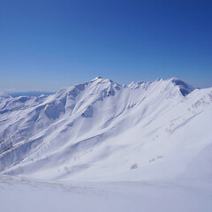 Majestic snow-capped mountains towering against a clear blue sky, with dramatic peaks and pristine landscapes under bright daylight.