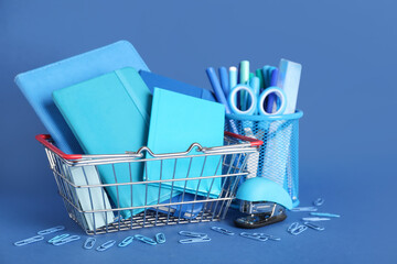 Small shopping basket with school supplies on blue background
