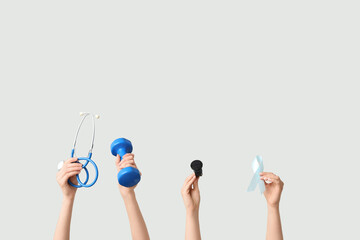 Female hands with stethoscope, dumbbell, wristwatch and light blue ribbon on white background....