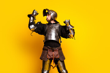 Young man humorously posing in a medieval knight armor against a bold yellow background