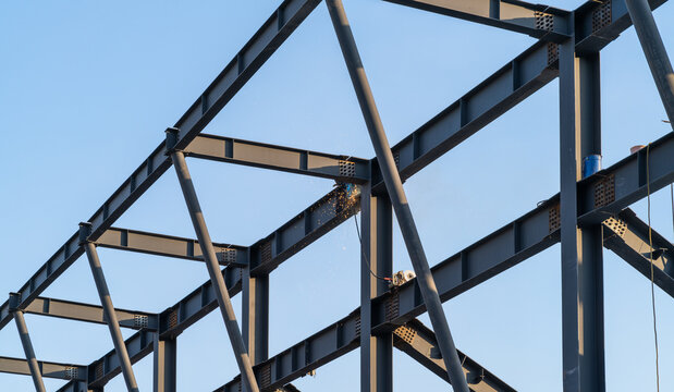 Welding process with bright sparks on a steel structure. Frame building under construction, where metal beams and columns are being connected. Industrial development in progress.