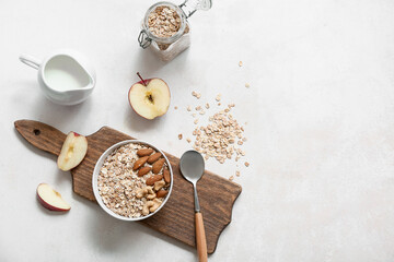 Wooden cutting board, apple, bowl and jar with raw oatmeal on light background