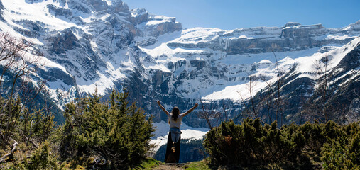 Beautiful young girl raising her arms facing the magnificent landscapes of the Cirque de Gavarnie,...