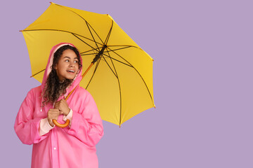 Happy young African-American woman in raincoat with umbrella on lilac background