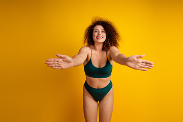 Young woman in green lingerie posing confidently against a vibrant yellow background, embracing natural beauty and self acceptance