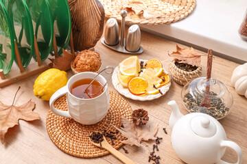 Teapot, cup of green tea near muffin, plate with lemon and autumn decor on table in room. Closeup