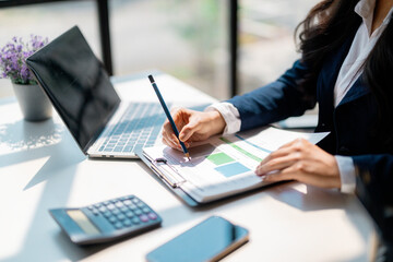 Businesswoman analyzing financial charts and taking notes in office