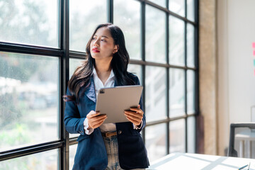 Businesswoman holding tablet and looking out window in modern office