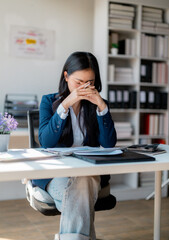 Stressed Asian businesswoman holding head in hands at office desk