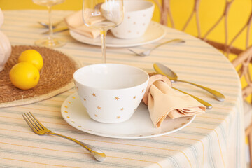 Stylish table setting decorated with fresh lemons near yellow wall in dining room