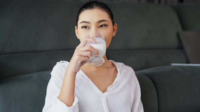 Young Asian woman enjoying drinking milk in a glass at the dining table in her home.