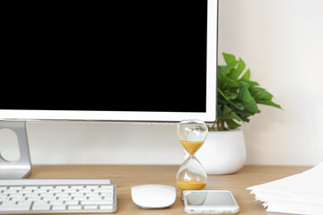 Hourglass with computer on desk in office, closeup