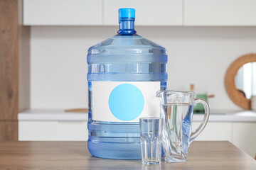 Bottle of clean water with jug and glass on table in kitchen